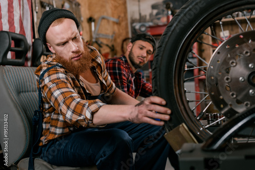 handsome mechanics examining wheel of motorcycle at garage