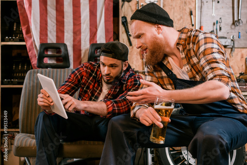 mechanics drinking beer and using tablet together at garage