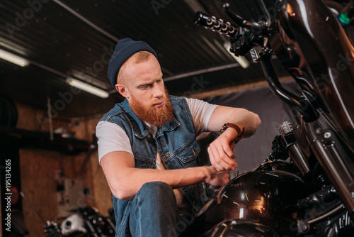 young man looking at watch while sitting on motorcycle at garage