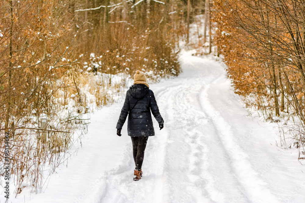 Naklejka premium Woman walking in snow at winter. Girl on snowy road in the forest.