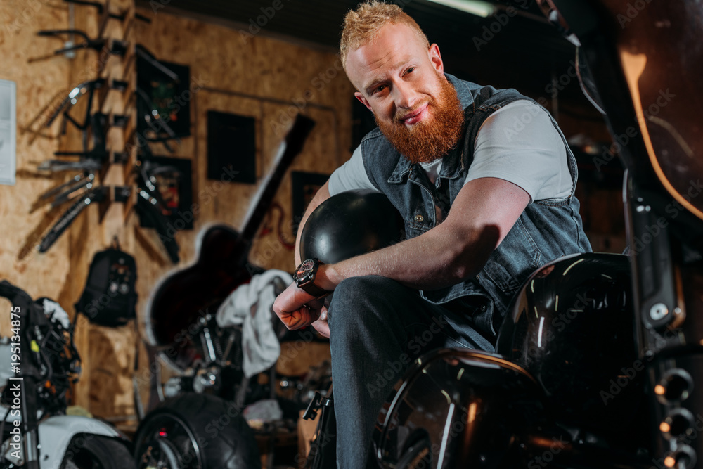 bearded young man sitting on bike with helmet at garage bearded young man sitting on bike with helmet at garage