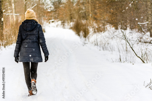 Woman walking in snow in winter clothes. Girl on snowy road in park.