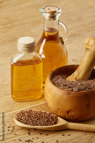 Beautiful composition of glass oil jars, wooden mortar and pestle with flax seeds, shallow depth of field, vertical.