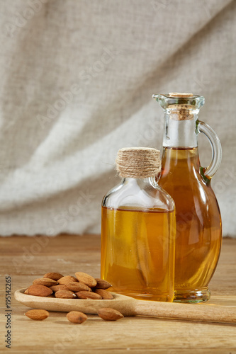 Aromatic oil in a glass jar and bottle with almond in a scoop on wooden table, close-up, vertical. photo