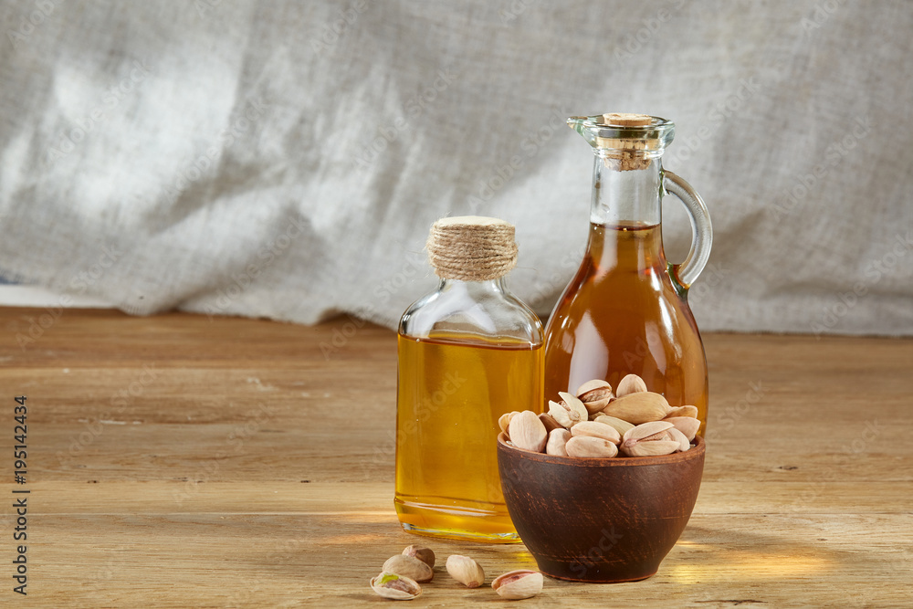 Aromatic oil in a glass jar and bottle with pistacios in bowl on wooden table, close-up. Aromatic oil in a glass jar and bottle with pistacios in bowl on wooden table, close-up.