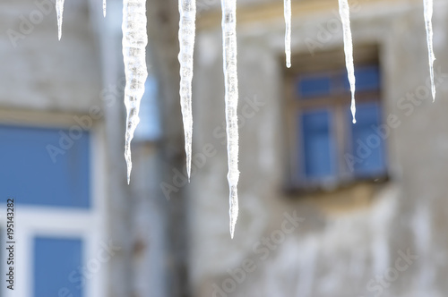 Frozen icicles on the roof against a background of blurry window © vizland