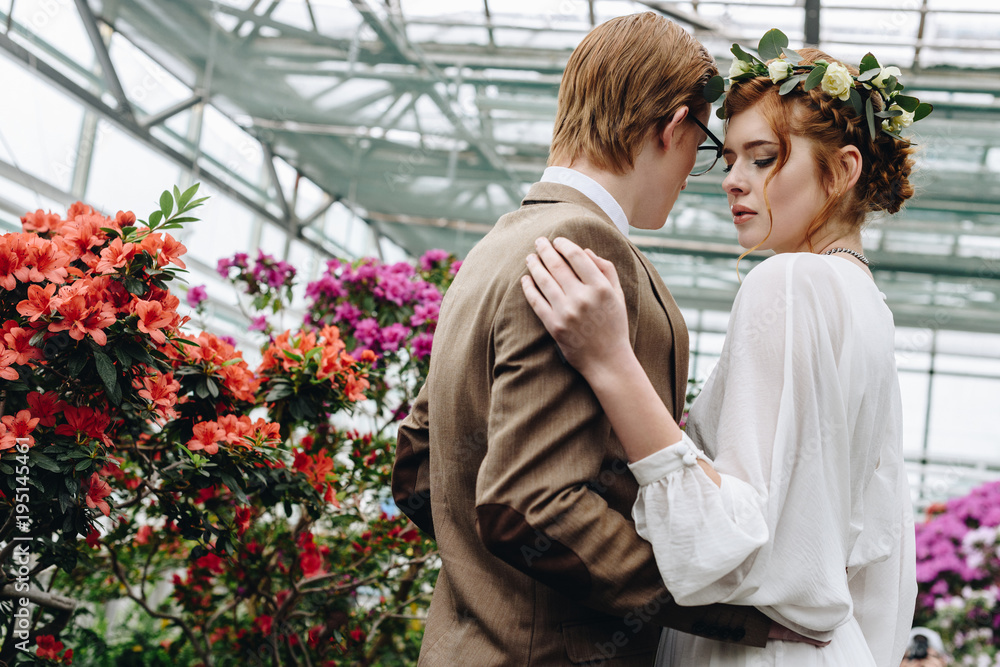 beautiful young elegant wedding couple embracing between flowers in botanical garden