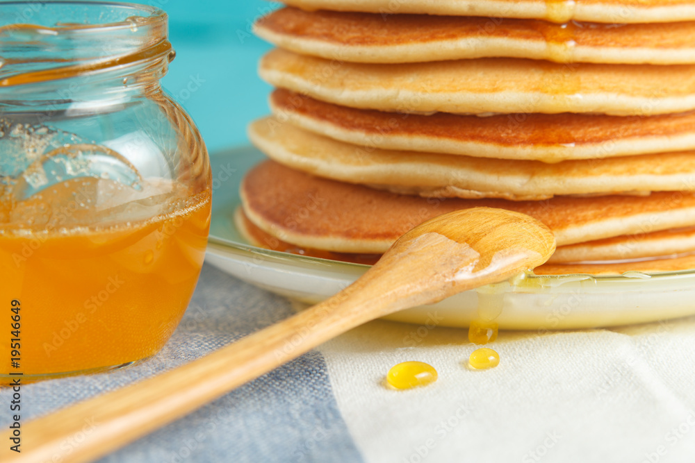 Fototapeta premium Close up of stack of pancake with pouring honey, wooden spoon and jar of honey