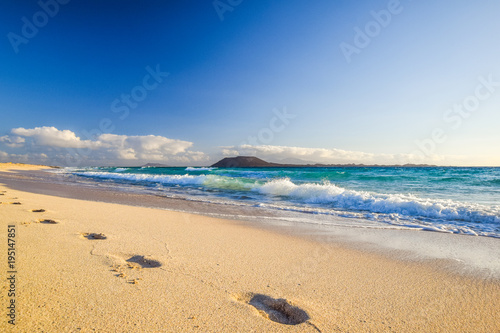 Fototapeta Naklejka Na Ścianę i Meble -  Stunning morning view of the islands of Lobos and Lanzarote seen from Corralejo Beach (Grandes Playas de Corralejo) on Fuerteventura, Canary Islands, Spain, Europe. Beautiful footprints in the sand.