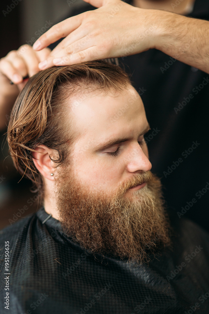 Obraz premium Barber using scissors and comb in barbershop