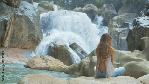 Girl Sits in Lotus Pose against Waterfall and Rocks photo