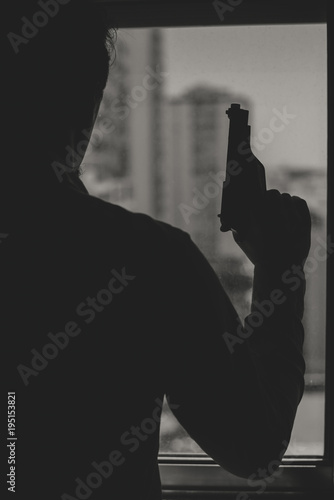 Black and white silhouette of man holding gun, window background