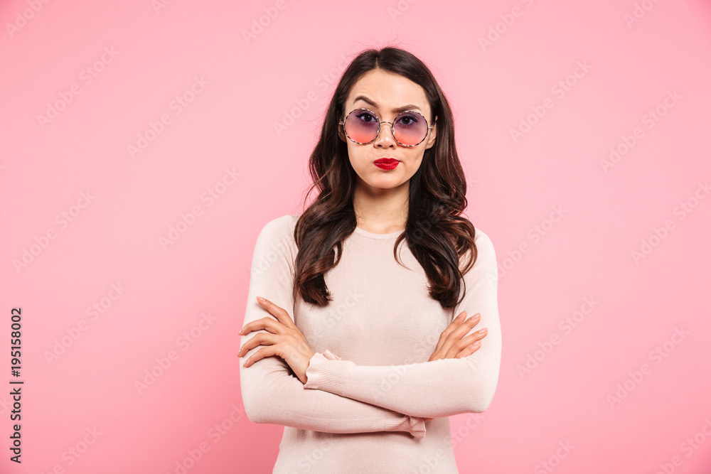 Photo of adult girl with brooding look and hands crossed looking on camera expressing resentment, isolated over pink background Photo of adult girl with brooding look and hands crossed looking on camera expressing resentment, isolated over pink background