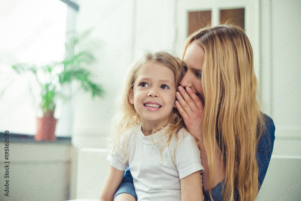Smiling and happy mom and daughter are hugging each other at home on the couch. Mom and daughter have fun. Smiling and happy mom and daughter are hugging each other at home on the couch. Mom and daughter have fun.