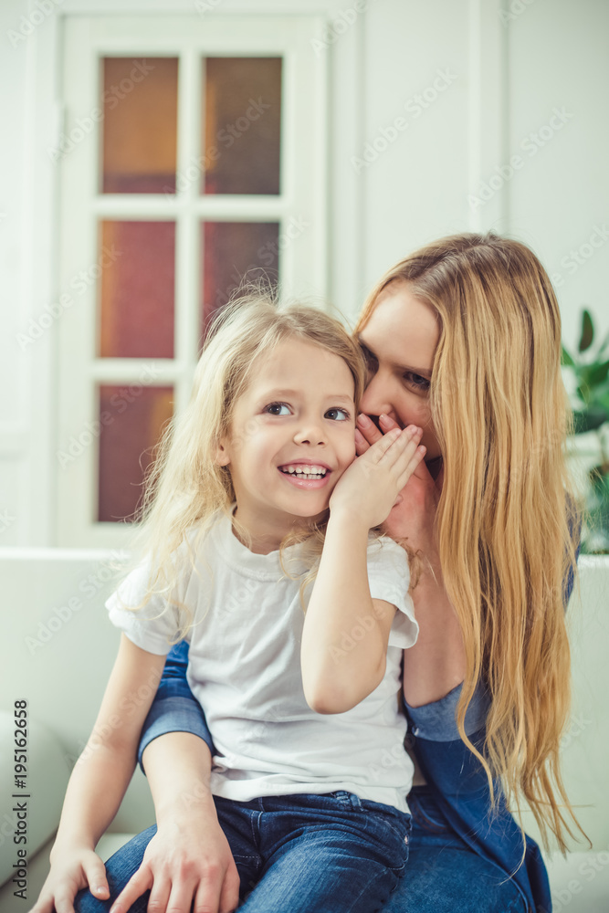 Smiling and happy mom and daughter are hugging each other at home on the couch. Mom and daughter have fun. Smiling and happy mom and daughter are hugging each other at home on the couch. Mom and daughter have fun.