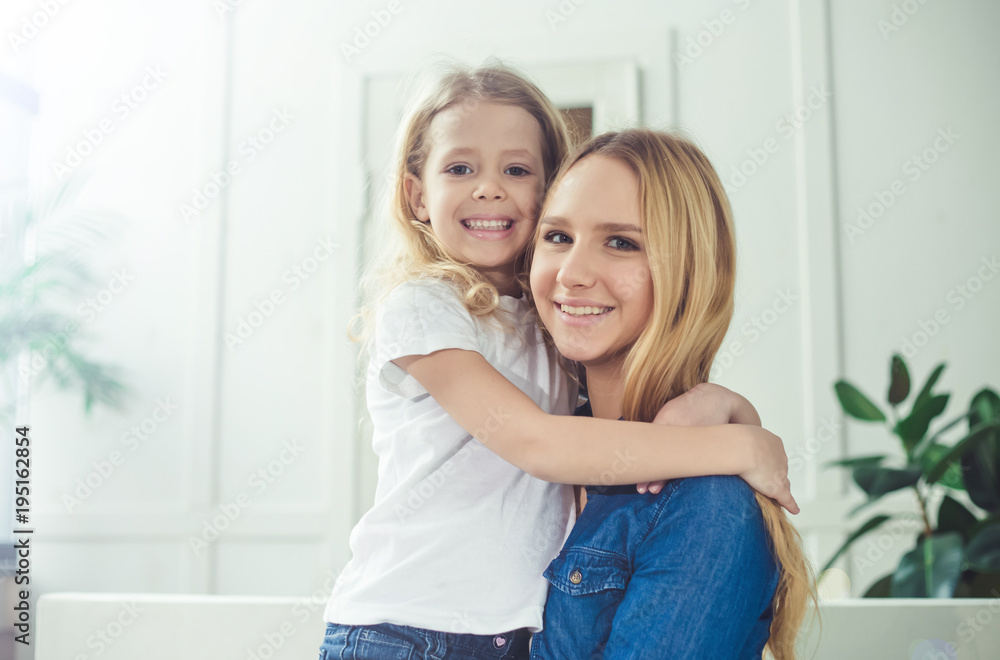 Smiling and happy mom and daughter are hugging each other at home on the couch. Mom and daughter  have fun. 
