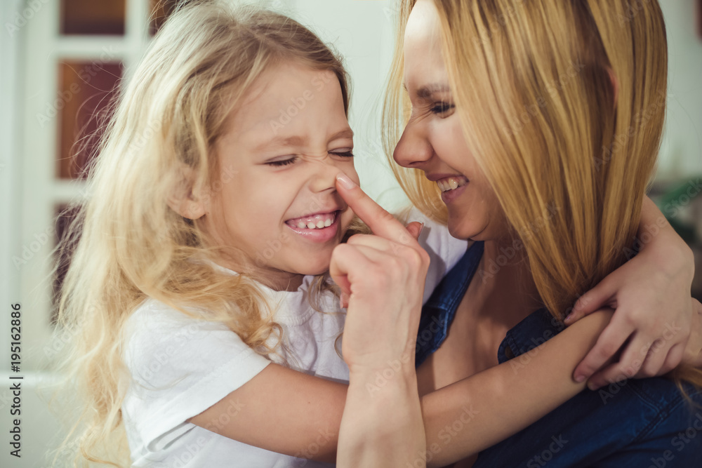 Smiling and happy mom and daughter are hugging each other at home on the couch. Mom and daughter have fun. Smiling and happy mom and daughter are hugging each other at home on the couch. Mom and daughter have fun.