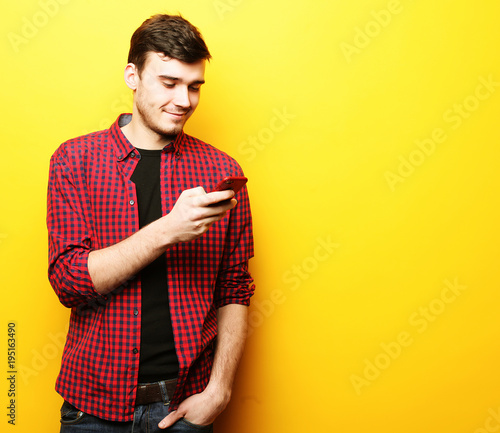 Happy young man talking on cell phone over yellow background