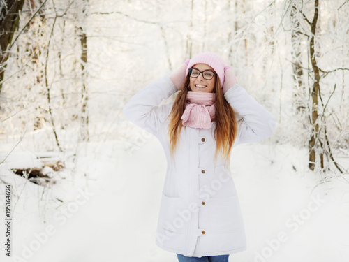 Adorable happy young blonde woman in pink knitted hat scarf having fun strolling snowy winter forest in nature photo