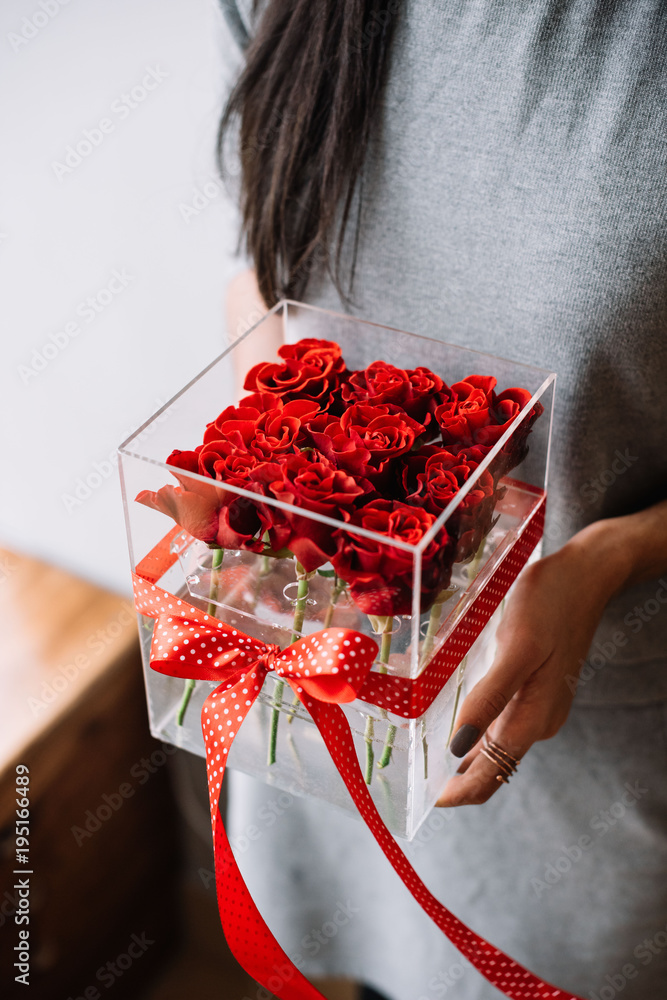 Fototapeta premium Woman holding transparent flower box filled with red roses with a red polka dotted bow on it