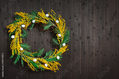 Wreath of mimosa with eggs on a brown background