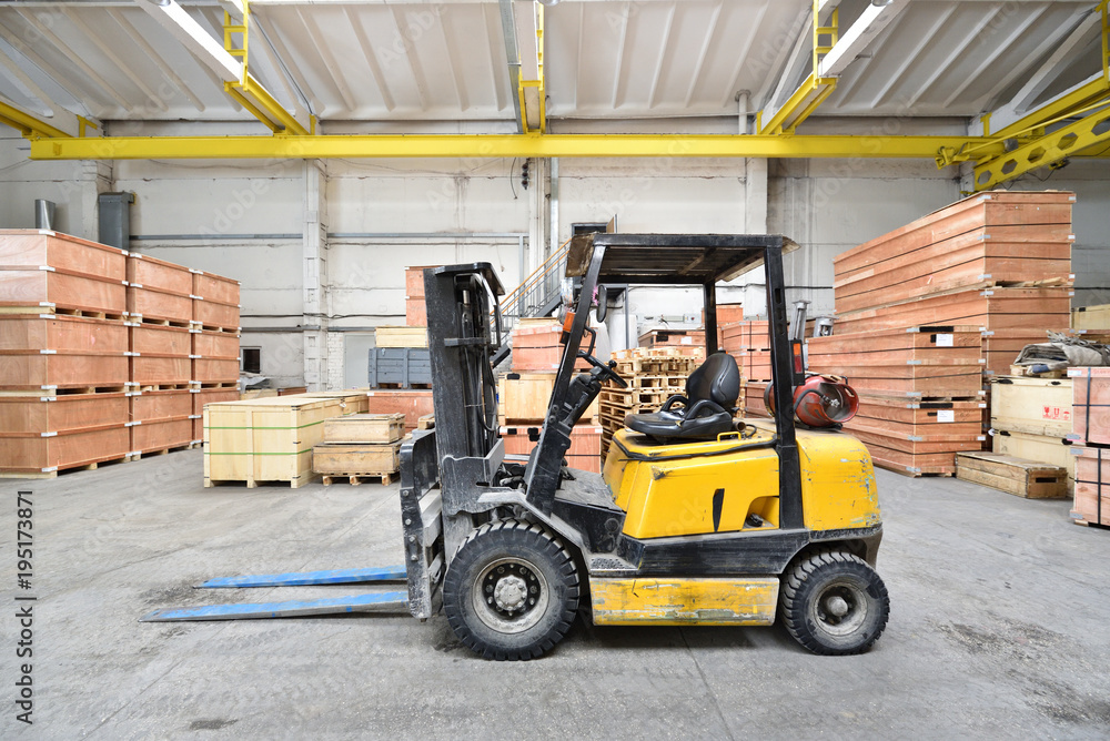 The forklift is old and scratched in a large and light warehouse. Yellow color