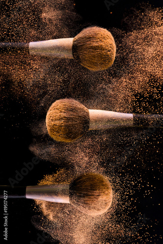 Three brushes for makeup with gold make-up shadows in motion on a black background.
