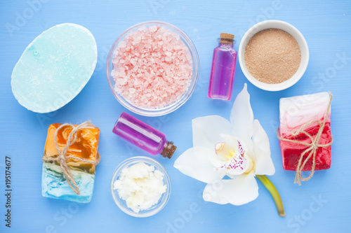 Spa and natural cosmetics concept. Set of sea salt, orchid, natural clay ,shea oil, glass bottles and other spa treatment tools on the blue wooden background. Top view. Space for a text. Close up.