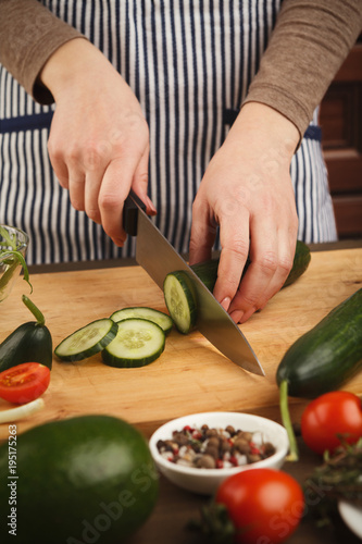 Woman cutting cucumber for fresh salad side view