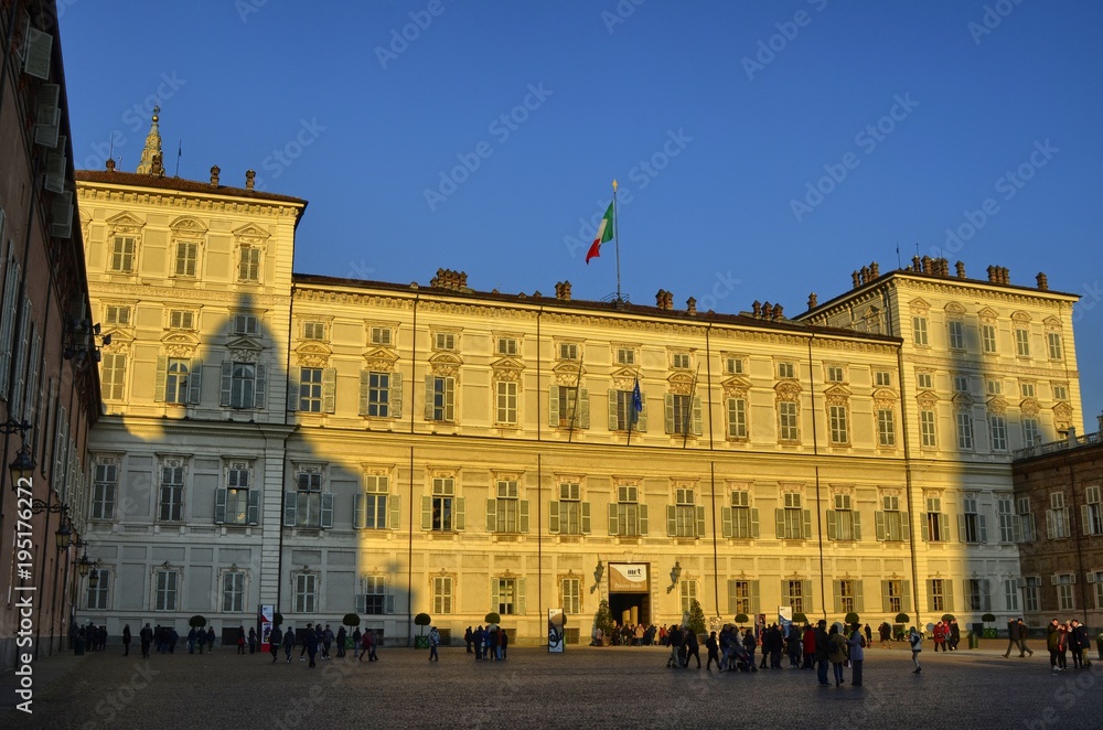 Turin, Italy, Piedmont, December 8 2017. The facade of the royal palace illuminated by the yellow light of the sun before sunset. Tourists visiting the city.