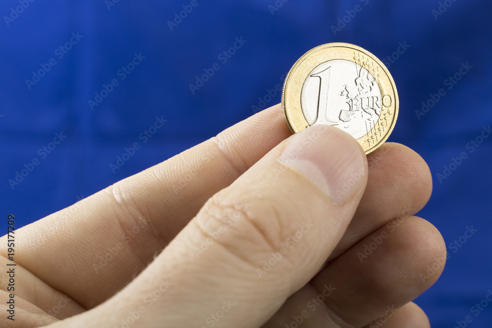 Close up of one Euro coin in the hand on the dark blue background Close up of one Euro coin in the hand on the dark blue background