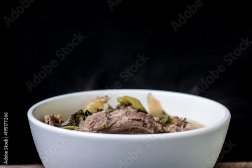 Pickled lettuce soup with spare rips in white bowl on wood and black background, Asian food, Dark tone