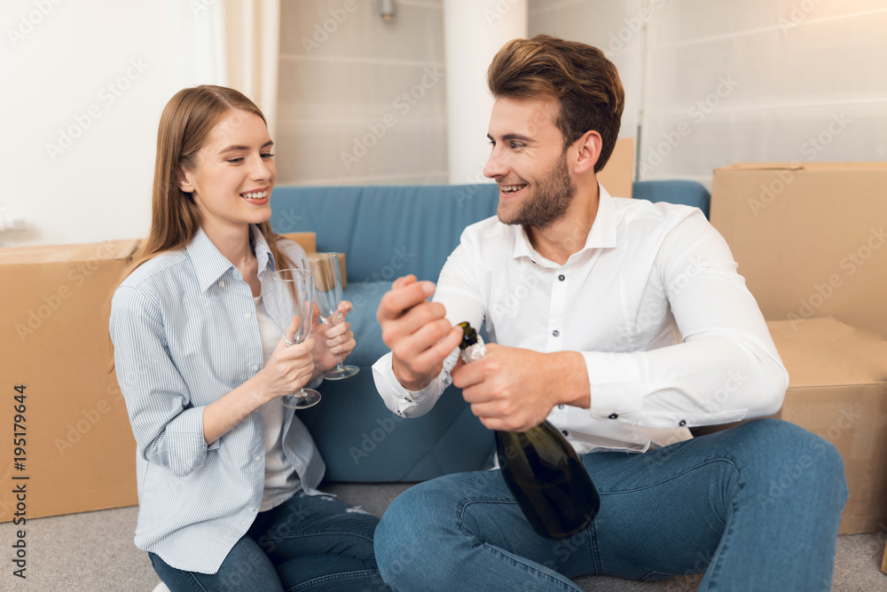 Young couple celebrating with champagne moving to new apartment. Moving newlyweds to new housing Young couple celebrating with champagne moving to new apartment. Moving newlyweds to new housing
