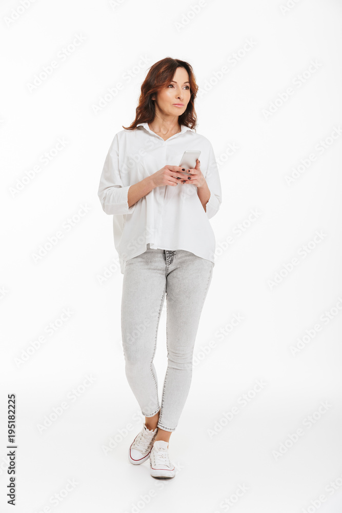 Full length portrait of elegant woman 40s holding smartphone and browsing internet or chatting, isolated over white background in studio Full length portrait of elegant woman 40s holding smartphone and browsing internet or chatting, isolated over white background in studio
