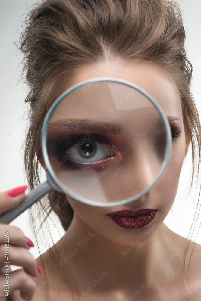 Beautiful naked shoulders girl looking through a magnifying glass and increases with it her beautiful eye Beautiful naked shoulders girl looking through a magnifying glass and increases with it her beautiful eye