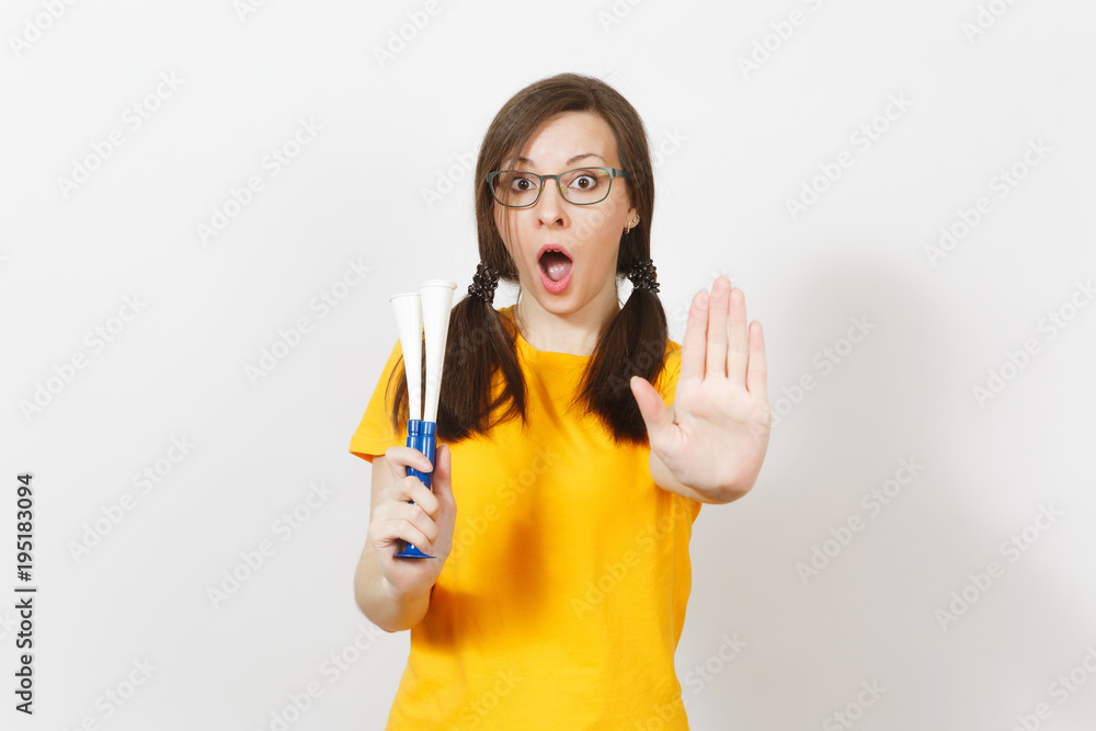 Beautiful European young woman with fun pony tails, fan or player in glasses, yellow uniform show stop gesture, hold football pipe isolated on white background. Sport fan, healthy lifestyle concept. Beautiful European young woman with fun pony tails, fan or player in glasses, yellow uniform show stop gesture, hold football pipe isolated on white background. Sport fan, healthy lifestyle concept.