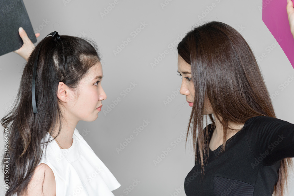 Businesswomen workmate has use a pink and black folder for hitting and fighting with angry and upset in the office isolated and grey background. Businesswomen workmate has use a pink and black folder for hitting and fighting with angry and upset in the office isolated and grey background.
