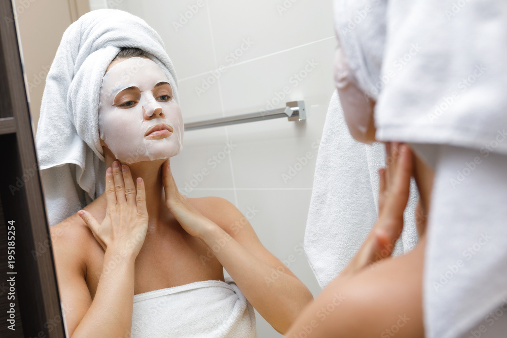 Woman in bathroom is applying facial sheet mask