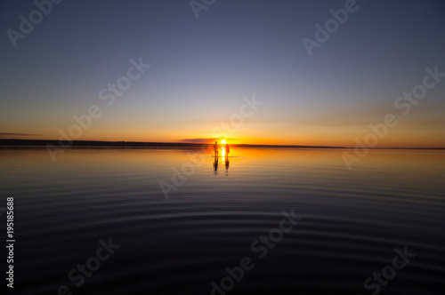 Young couple is walking away in the water on summer beach. Sunset over the sea.Two silhouettes against the sun. Just married couple in romantic love story. Man and woman in holiday honeymoon trip.