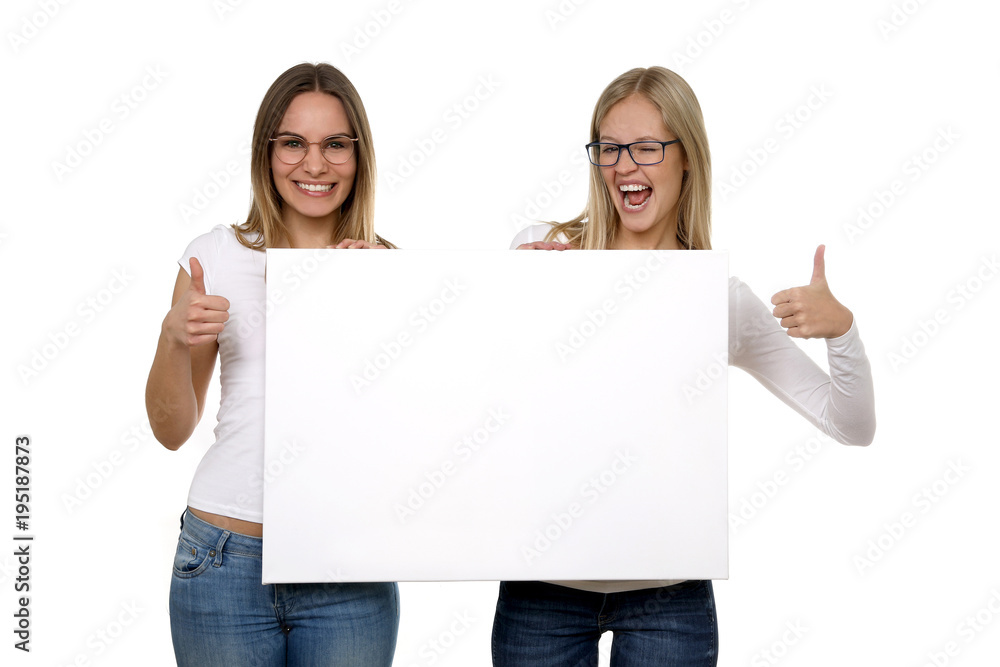 Zwei hübsche blonde Frauen mit Brille begeistert halten eine leere Tafel in ihren Händen und Daumen hoch Zwei hübsche blonde Frauen mit Brille begeistert halten eine leere Tafel in ihren Händen und Daumen hoch