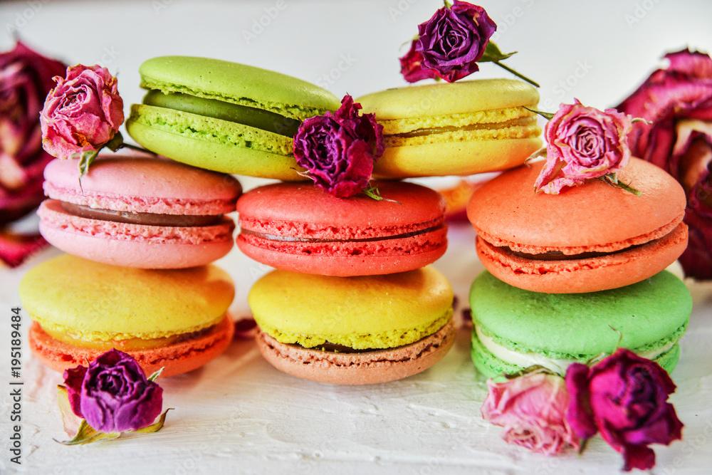 Dessert: A Delicate Fresh Colorful French Macaroons In Pastel Colors With Flowers Roses On A Light Textile Background, Top View Dessert: A Delicate Fresh Colorful French Macaroons In Pastel Colors With Flowers Roses On A Light Textile Background, Top View