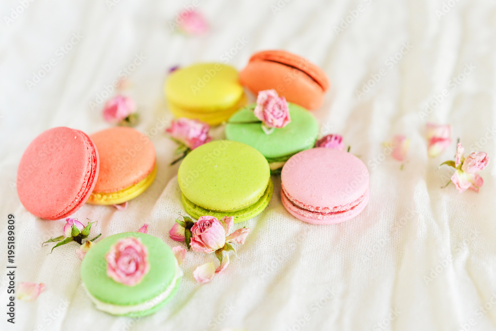 Delicate Fresh Colorful French Macaroons In Pastel Colors With Flowers Roses On A Light Textile Background, Top View