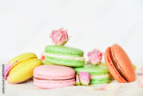 Dessert: A Delicate Fresh Colorful French Macaroons In Pastel Colors With Flowers Roses On A Light Textile Background, Top View
