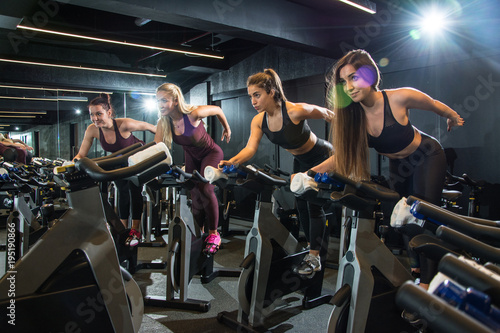 Group of fitness girls riding exercise bikes together on cycling class at gym.