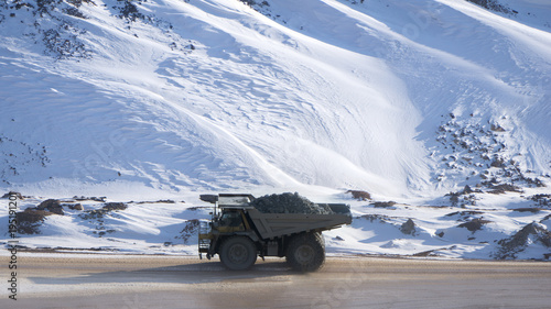 Dump truck loaded with ore driving through a snow covered open pit mine
