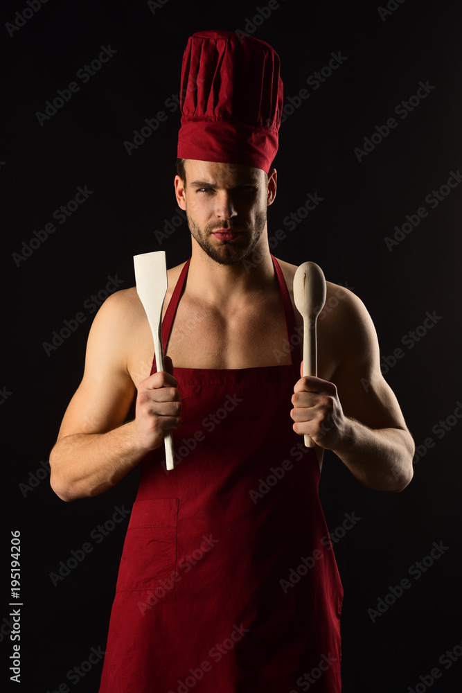 Kitchen utensils concept - serious bearded man in cook hat and apron with  wooden kitchen spatula and