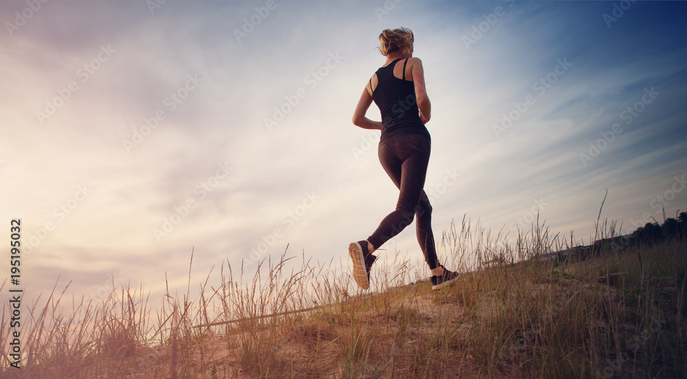 Young woman running on the field near seaside at sunset. Active person outdoors at the dusk in summer Young woman running on the field near seaside at sunset. Active person outdoors at the dusk in summer