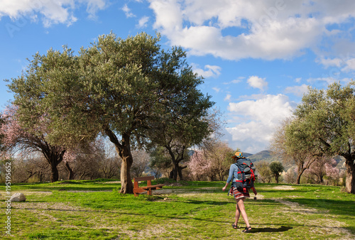 A young girl with a big backpack goes to rest on a bench under the old olive tree