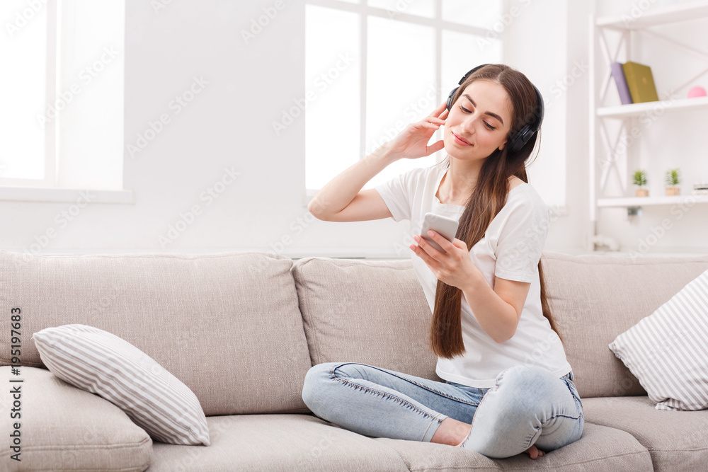 Young woman with cell phone and headphones on beige couch Young woman with cell phone and headphones on beige couch