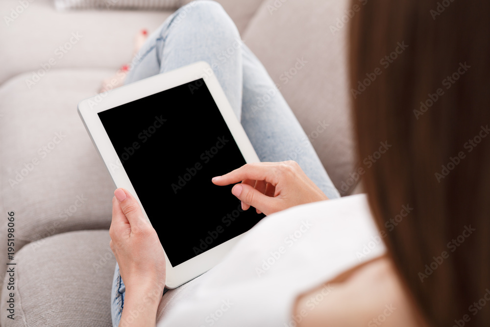 Unrecognizable brunette girl with tablet sitting on the sofa